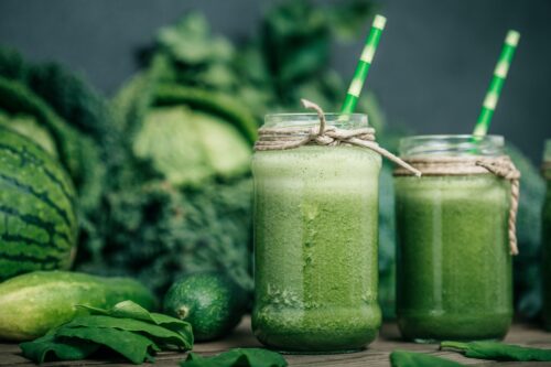 Blended green smoothie with ingredients on wooden table